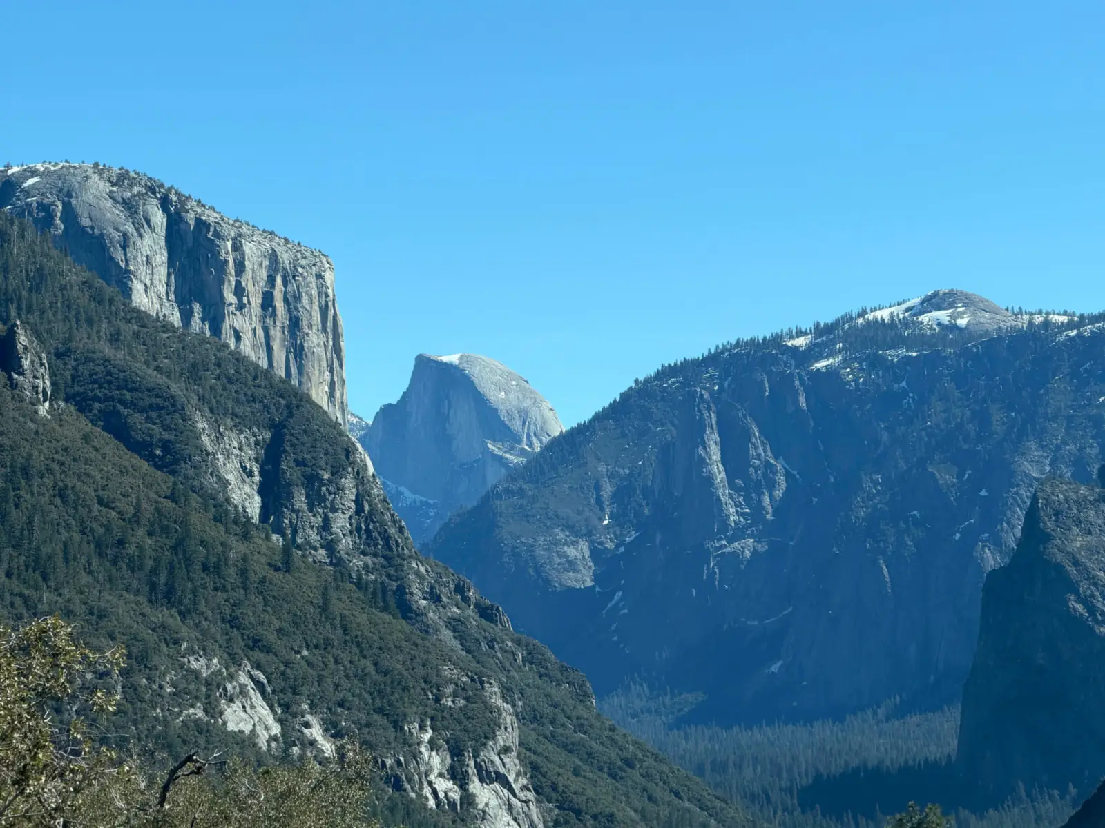 A granite valley with a sheer cliff on the left and a distant dome under a blue sky.